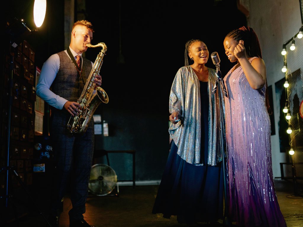 Hombre saxofonista tocando en un evento junto con dos jóvenes cantantes